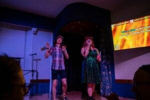 Two people on stage at Edinburgh Deaf Festival's Def Karaoke event. One is signing while the other is singing.