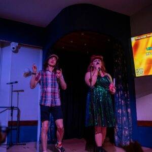 Two people on stage at Edinburgh Deaf Festival's Def Karaoke event. One is signing while the other is singing.