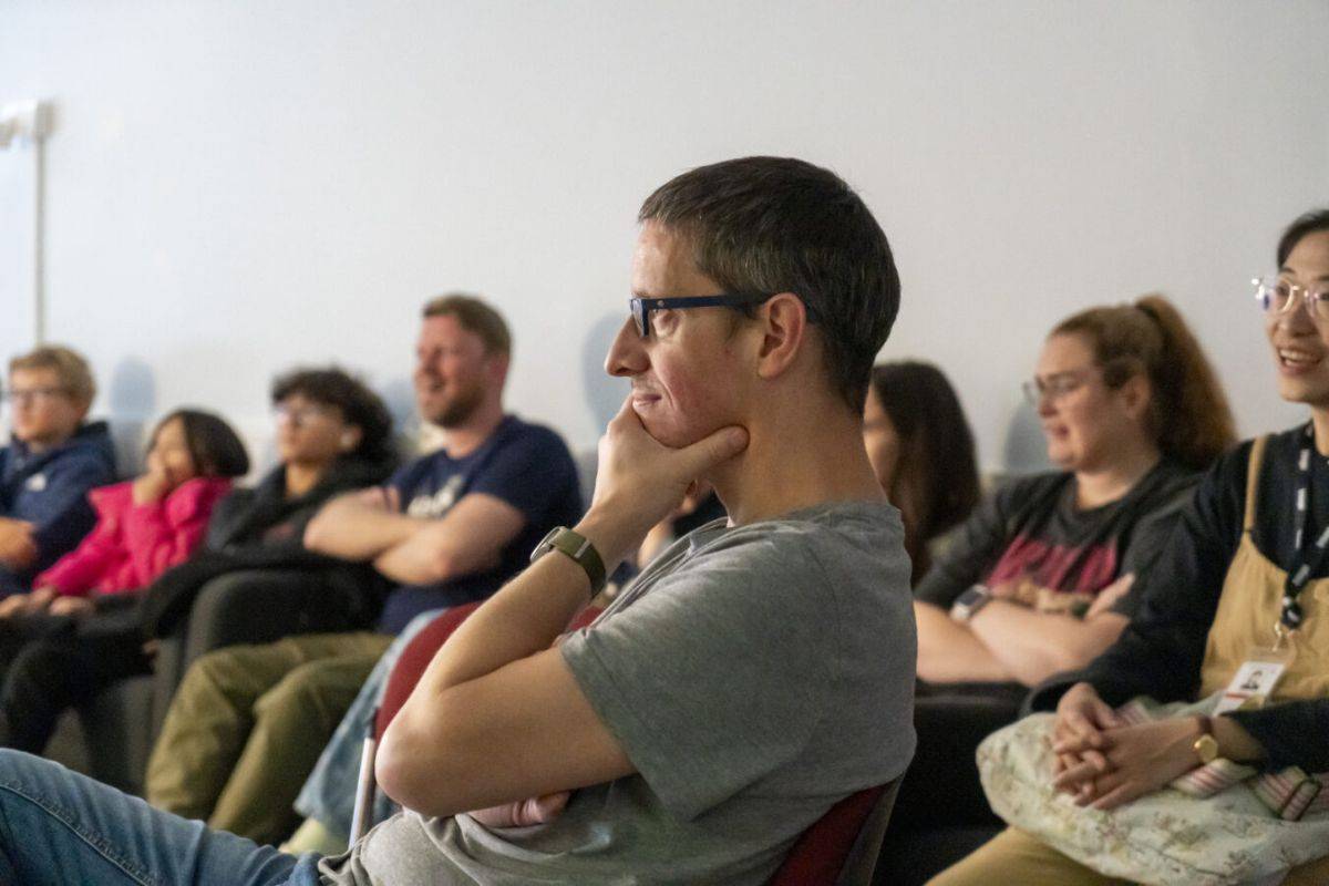 A man sits with his hand on his chin looking towards a presenter. Behind him are a number of people also looking towards a presenter.