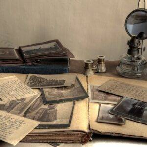 A collection of old papers and photographs on a table. Old archived books and a magnifying glass also lie on the table.