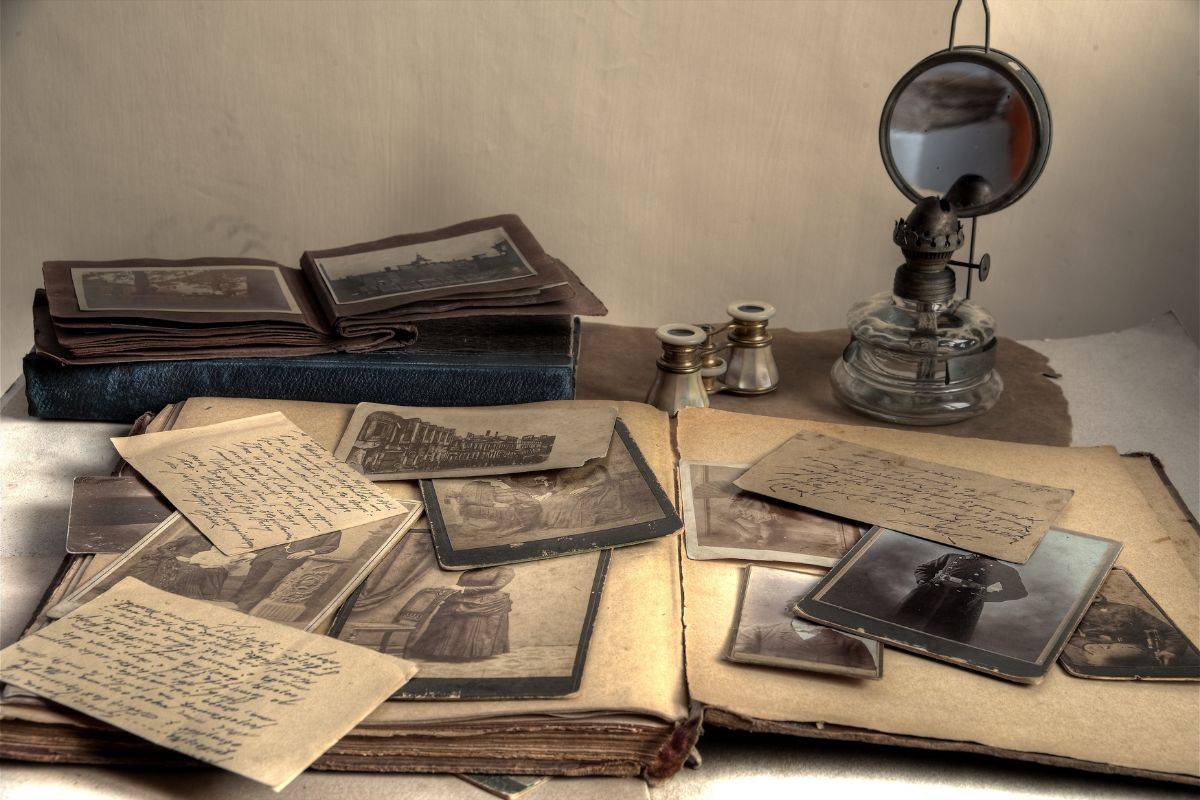 A collection of old papers and photographs on a table. Old archived books and a magnifying glass also lie on the table.