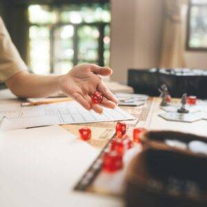 Someone playing Dungeons and dragons on a table using red dice.