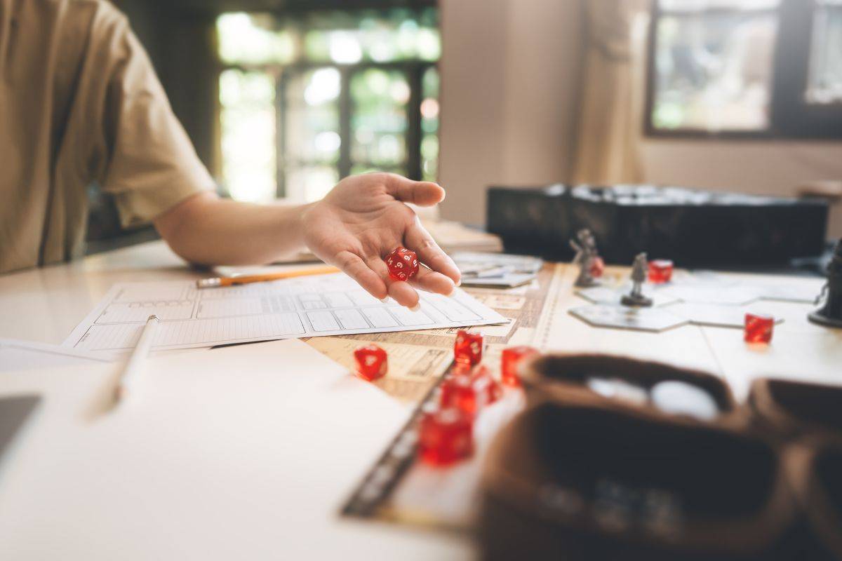 Someone playing Dungeons and dragons on a table using red dice.
