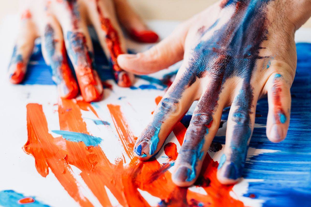 Hands on a piece of paper covered in blue and orange paint.