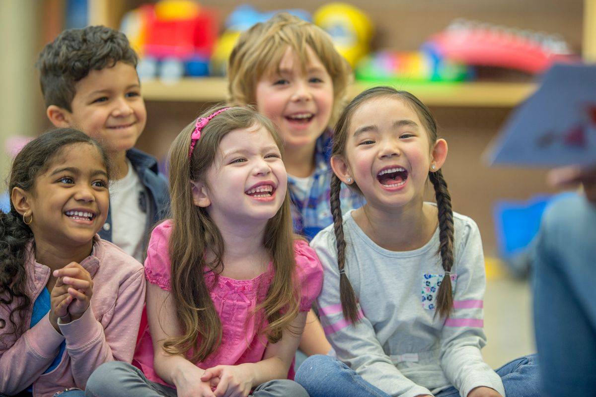 A group of children sit on the ground listening to a storyteller.