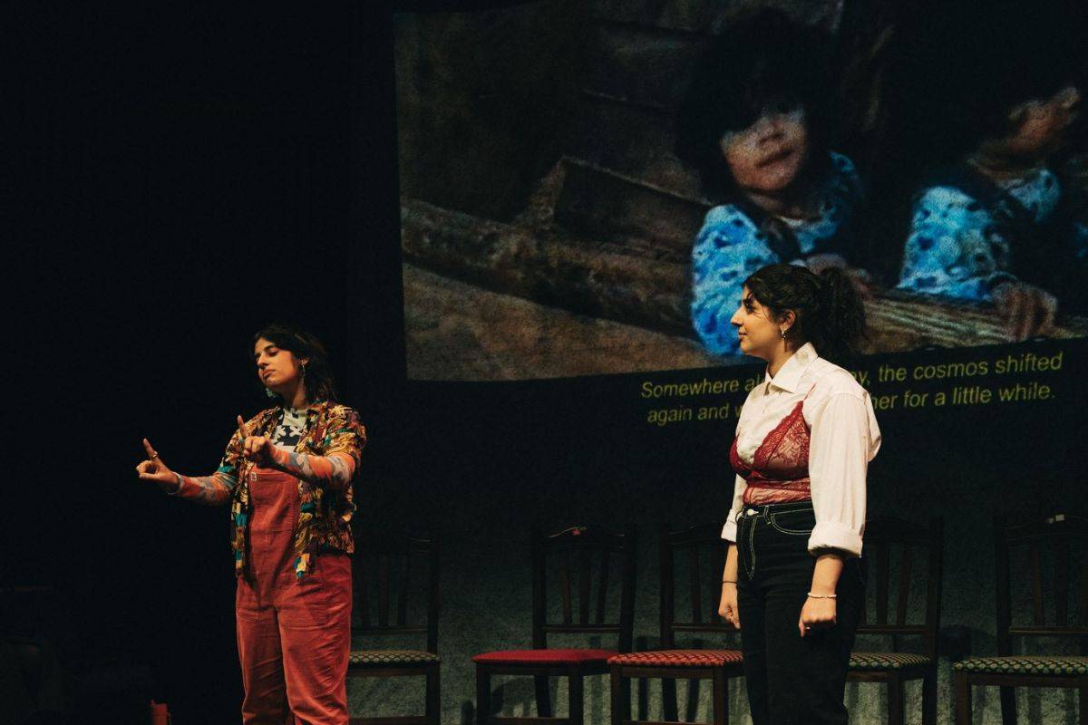 Mae and Fae Al-Kalamchi performing on stage together. Behind is an image of a young child projected onto the screen.