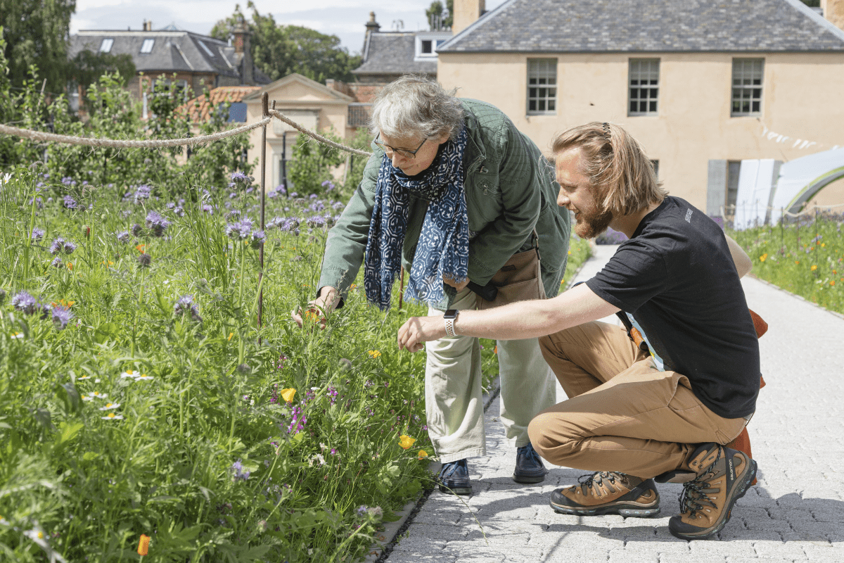 Two people at Royal Botanic Garden Edinburgh kneeling down to feel some flowers.