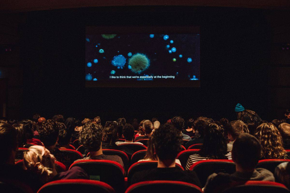 A cinema screen full of people watching a film on screen.