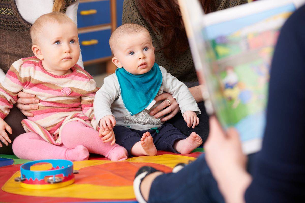 Two small children sit whilst someone reads from a storybook.