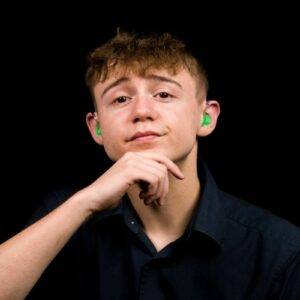 A photo of a young man with his hand on his chin, he is wearing hearing aids in both ears.