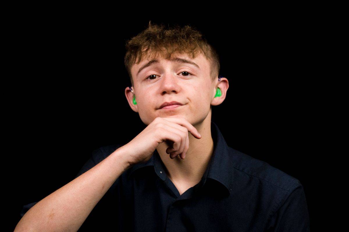 A photo of a young man with his hand on his chin, he is wearing hearing aids in both ears.