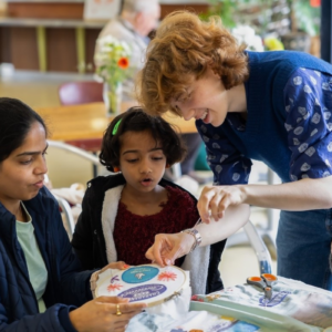 People being shown how to embroider in a workshop setting.