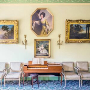 A georgian room with paintings on the wall, a desk and four chairs.