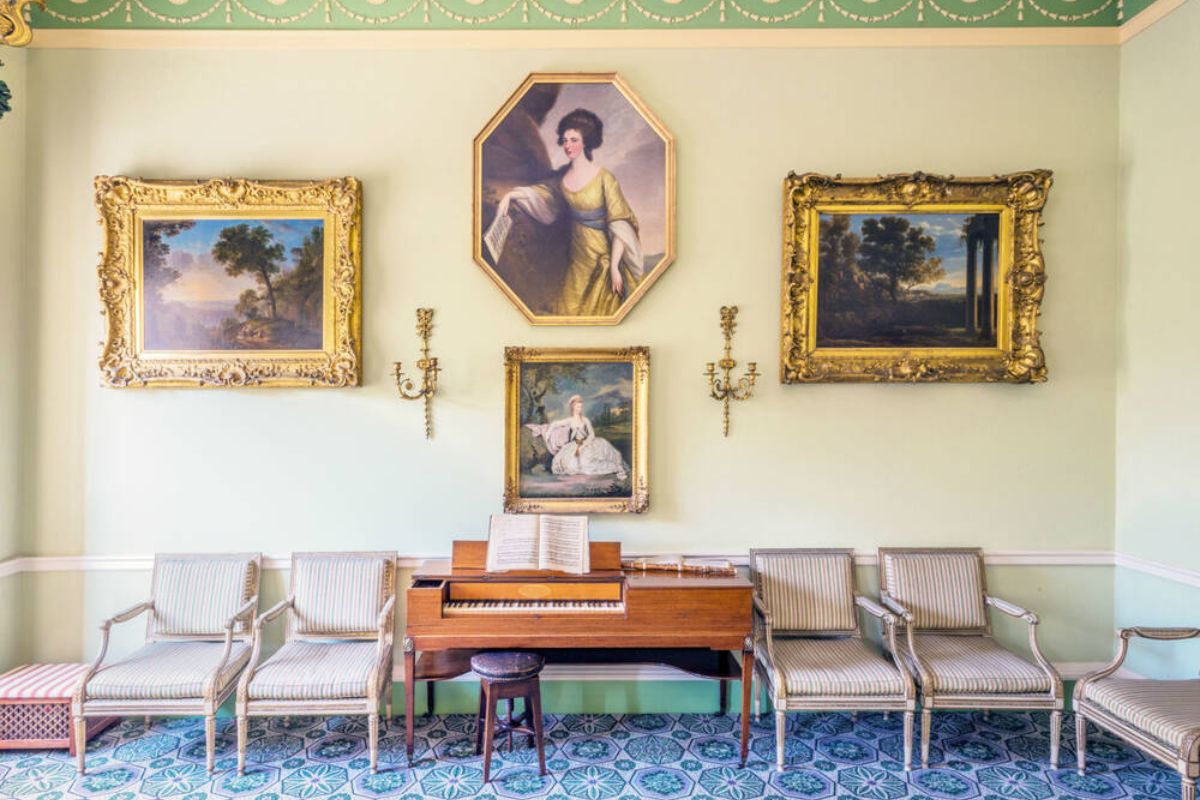 A georgian room with paintings on the wall, a desk and four chairs.