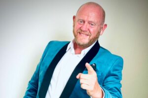 John smith in a blue velvet jacket pointing at the camera.
