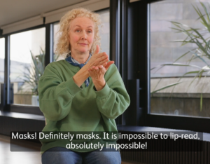 A woman in a green shirt sitting down using sign language to communicate.