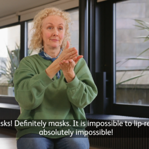 A woman in a green shirt sitting down using sign language to communicate.