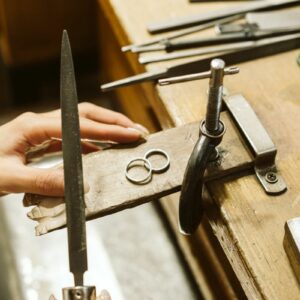 A silver ring on a workbench with someone holding tools