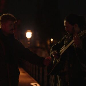 Two men standing beside each other, one is holding a guitar.